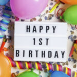 Happy 1st birthday celebration message on a lightbox with balloons and confetti